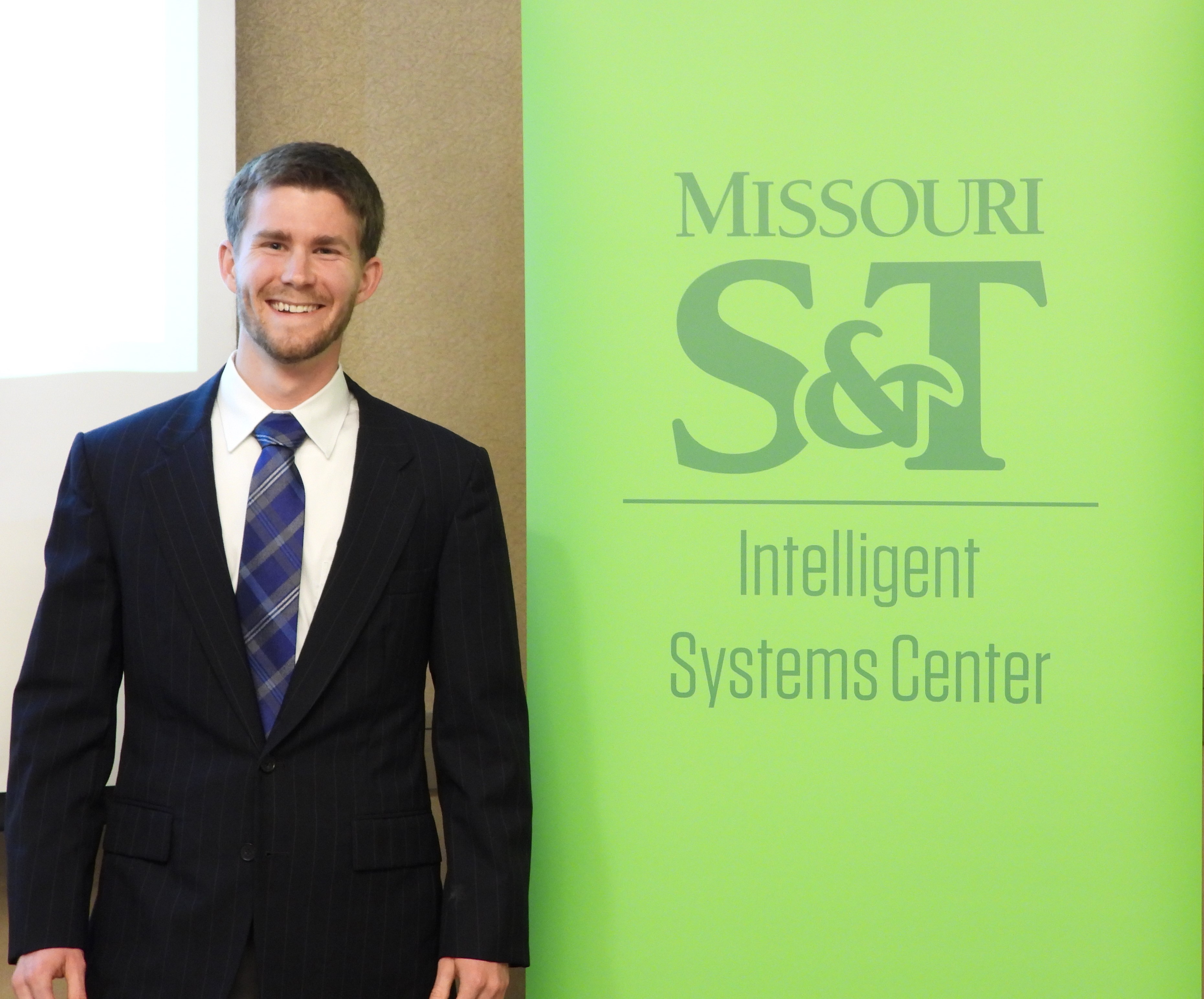First place winner, Jonathan Kelley, smiling next to Intelligent Systems Center banner.